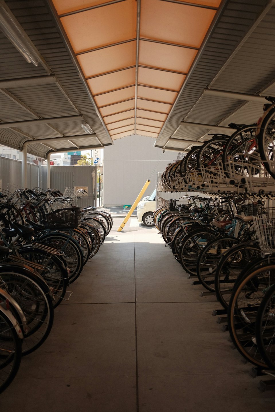 Många cyklar parkerade i ett utomhustak för cykelställ.
